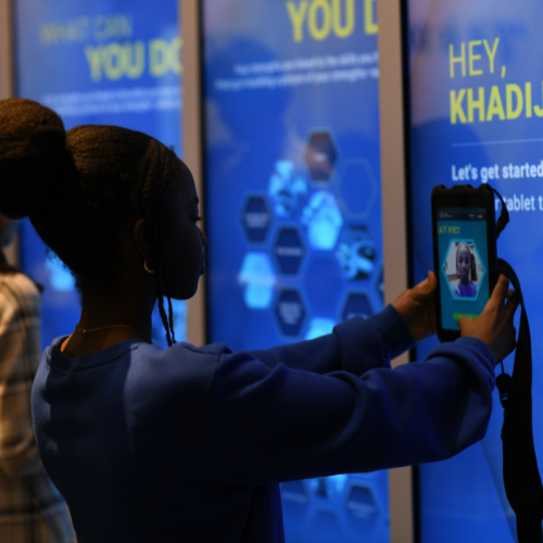 Person in blue shirt using a digital device in front of a glowing interactive display.