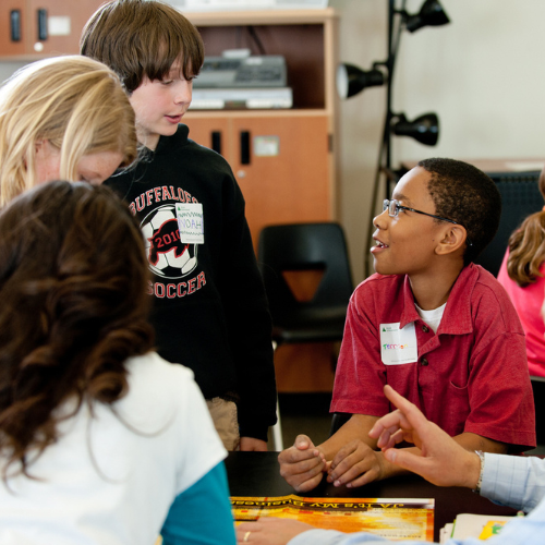 A group of children engaged in a lively classroom discussion around a table.